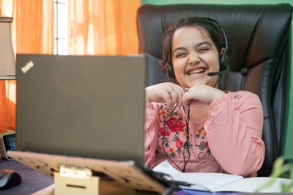 A young student seated at their desk, wearing a headset and laughing