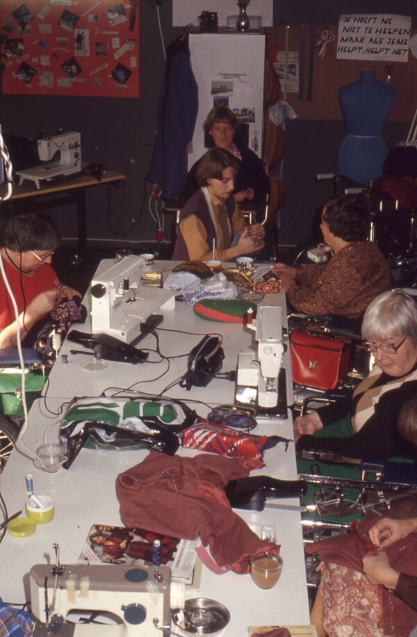 Image 2: Digitised slide of a group of Het Dorp residents and employees of the Sewing Ring around a large table filled with sewing machines and couture materials. Date unknown [1977-1985]. Property of Siza.